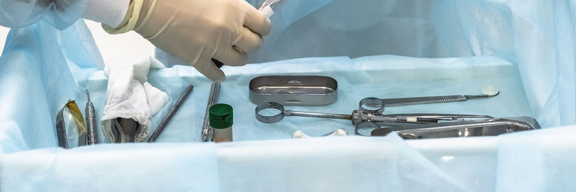 The image shows a person wearing medical gloves and a surgical mask, performing a procedure on a table covered with sterile drapes, with various medical instruments visible.