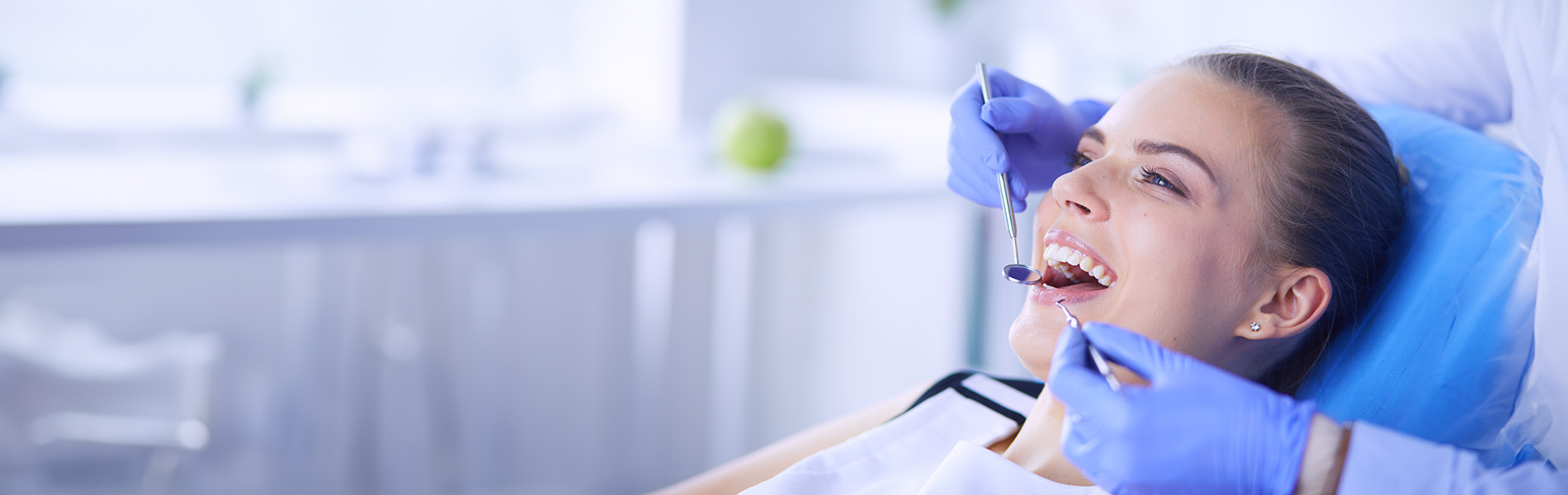 A woman wearing a surgical mask and holding a medical device over her mouth while seated in a dental chair.