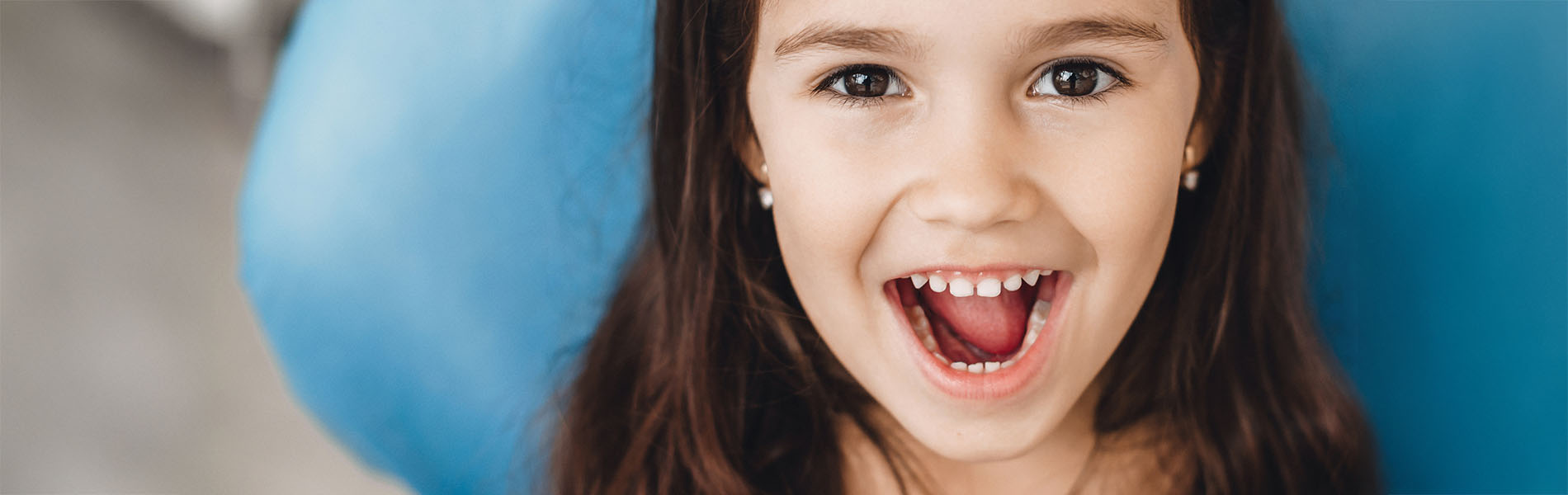 A young girl with her mouth open, appearing joyful or surprised, with a blue object behind her.