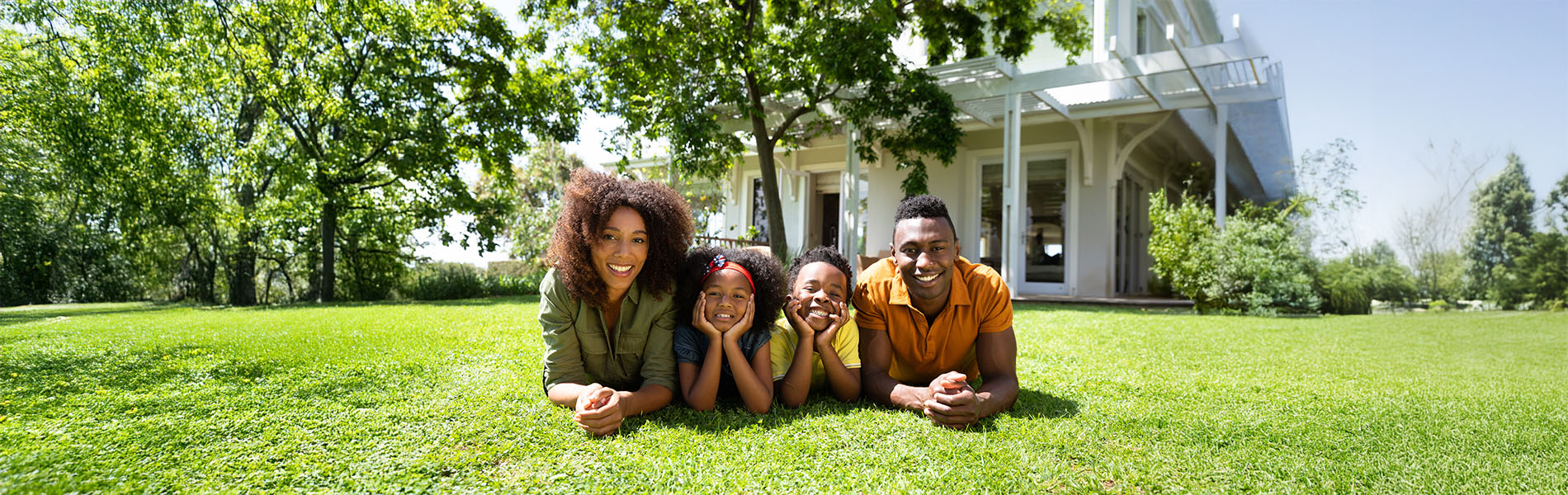 The image depicts a family of three sitting on grass in front of a church building under blue skies.