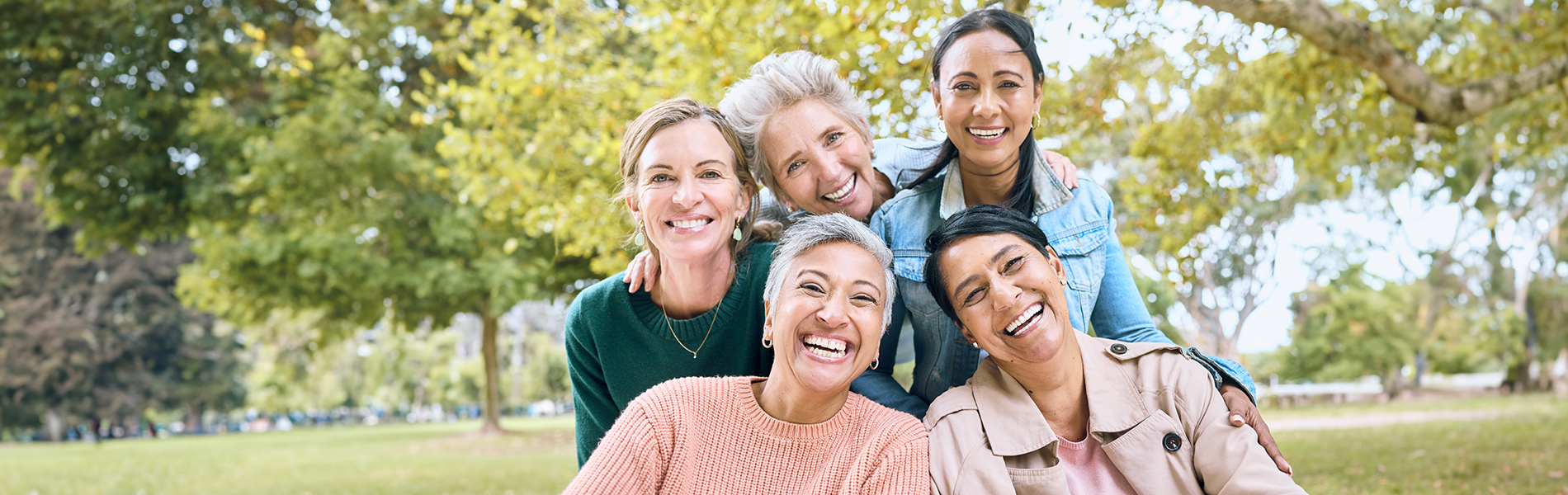 The image shows a group of six people smiling and posing together outdoors during daylight.
