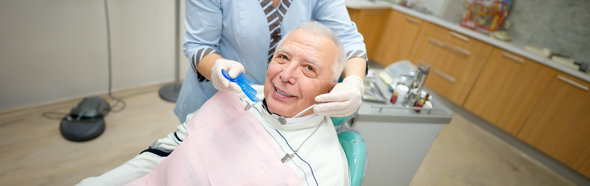 A person is seated in a dental chair, receiving care from a dental professional who stands behind them.