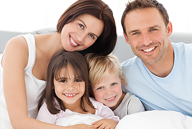 A family of four posing together on a bed with a happy expression.