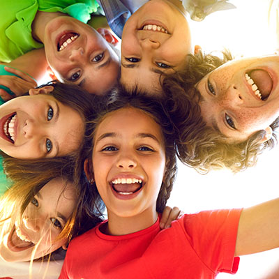 The image shows a group of children, likely friends, posing together with smiles on their faces, creating a circular formation around the camera s viewpoint.