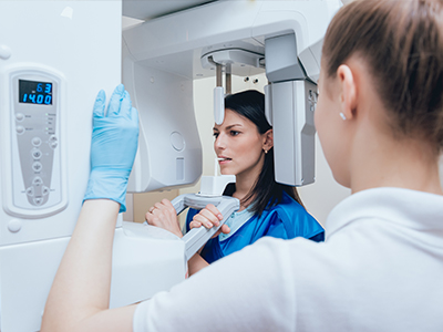 A woman in a blue lab coat is standing next to a large, modern 3D scanner with a digital display showing the word  scan  and a timer reading  0 42,  while another person in a white lab coat is observing the scan.