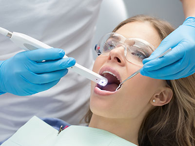 An individual receiving dental treatment with a dentist using a digital device to examine their mouth.